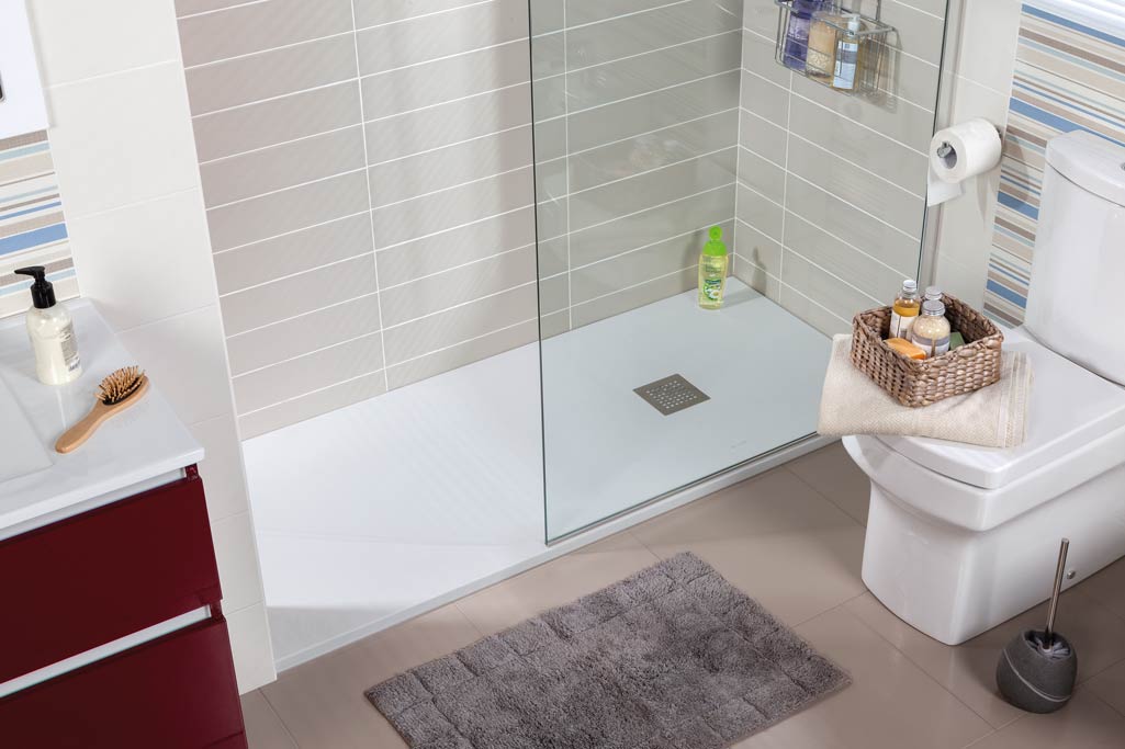 Plato de ducha GRIP en baño con azulejos grises y bote de jabón verde.