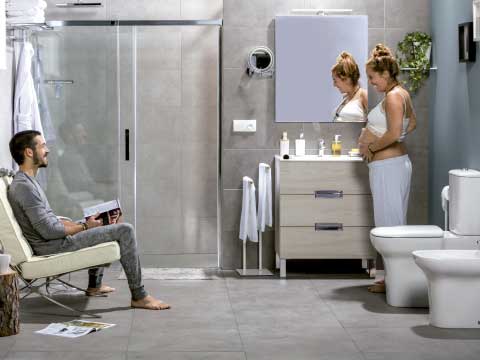Cuarto de baño que crece contigo donde aparece una pareja. Ella está embarazada y él mira una revista.